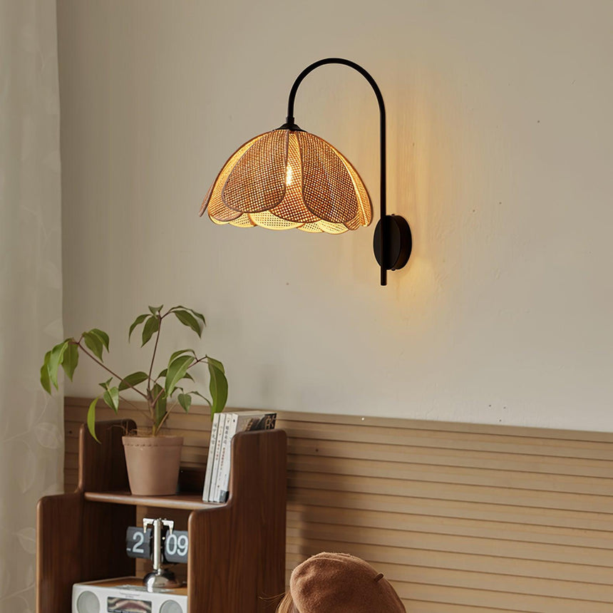 The rattan sconce lit above a low wood shelf with a plant and books