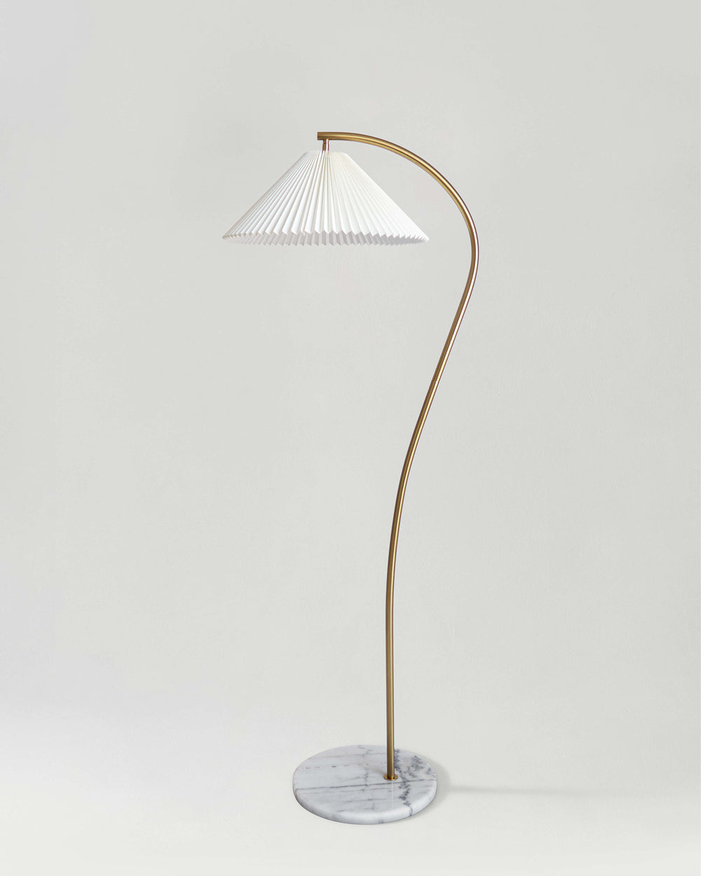 Brass floor lamp with a curved stem and a white pleated shade on a marble base