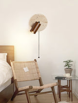 Sconce lit beside a cane chair and a side table holding a small plant