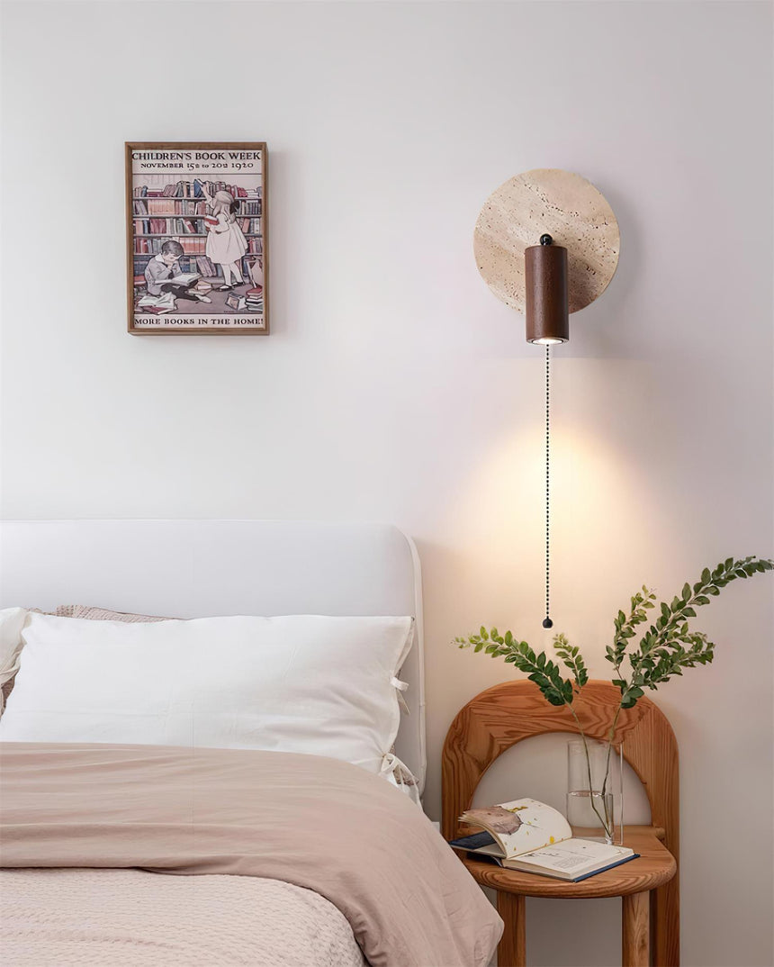 Sconce lit beside a framed print above a bed and a vase of branches