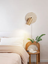 Sconce lit beside a bed above a cane nightstand holding a potted fern