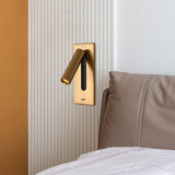 The gold reading light set into a wall beside a leather headboard and a bed