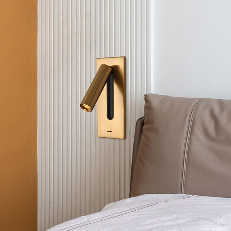 The gold reading light set into a wall beside a leather headboard and a bed