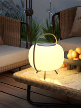The lamp lit on a woven bench with cushions and a planter behind it