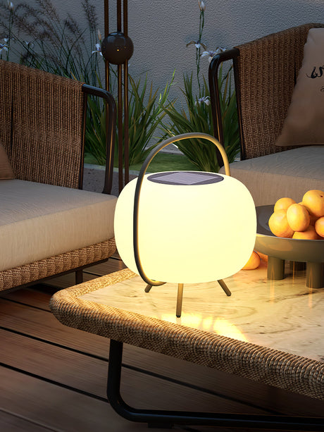The lamp lit on a woven bench with cushions and a planter behind it