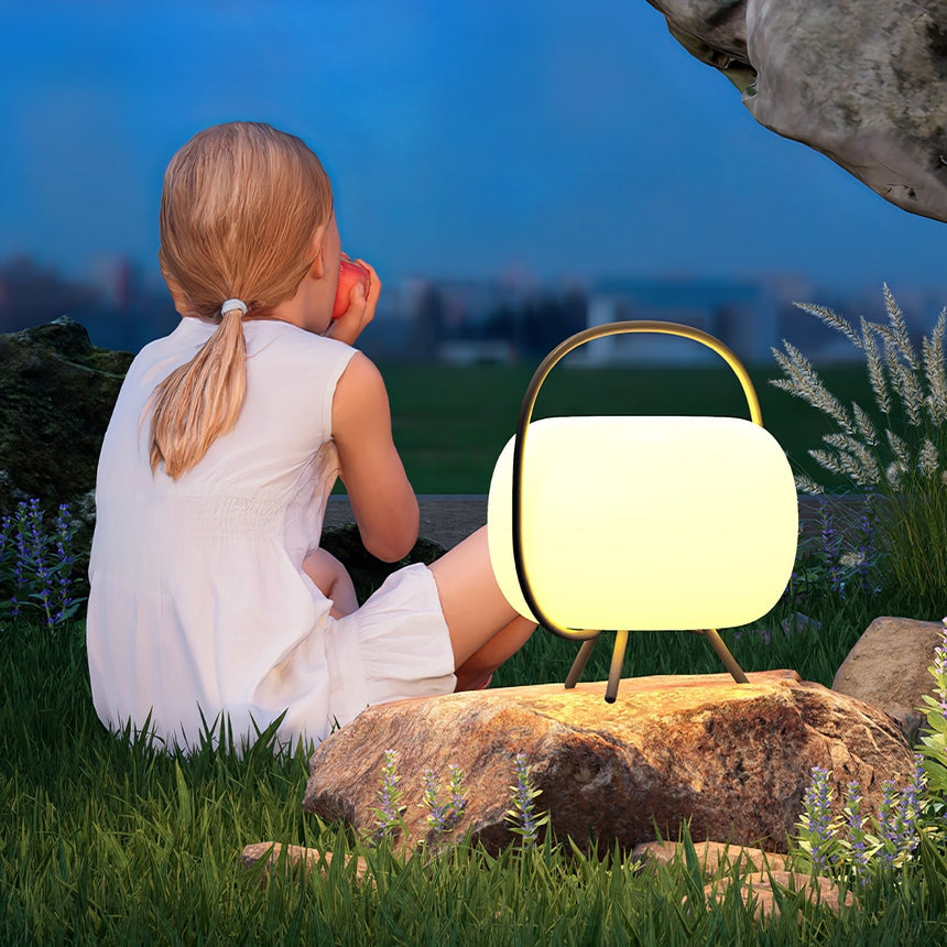 A child sitting on a lawn beside the lit lamp resting on a rock