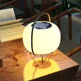 The lamp lit on a timber garden table beside an open book at night