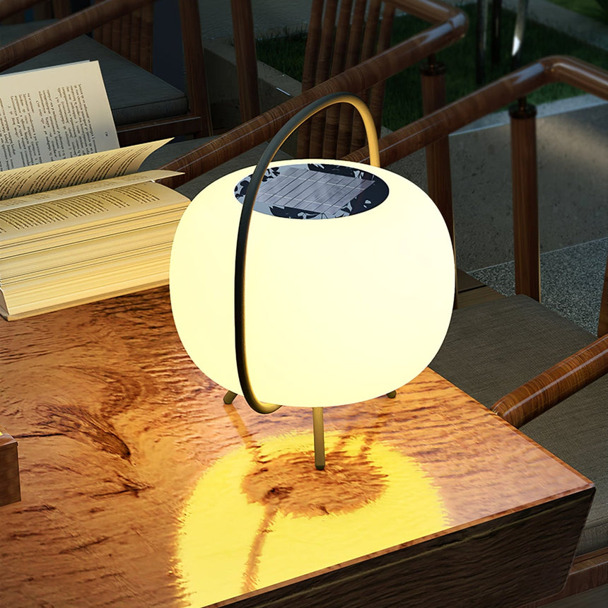 The lamp lit on a timber garden table beside an open book at night