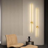 Two gold rods lit on a fluted wall beside a tan armchair and a footstool