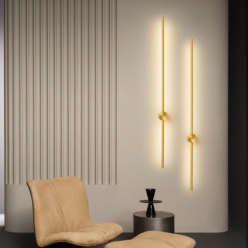Two gold rods lit on a fluted wall beside a tan armchair and a footstool