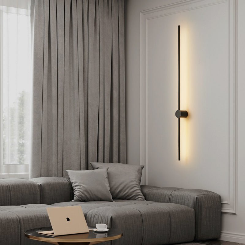 Lit beside a gray sofa with a laptop on a side table and a long curtain behind