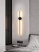 Mounted vertically beside a bed, the bar lit against a pale bedroom wall