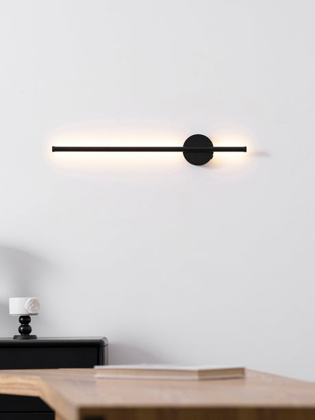 Lit warm above a nightstand, the beam falling onto the books stacked there