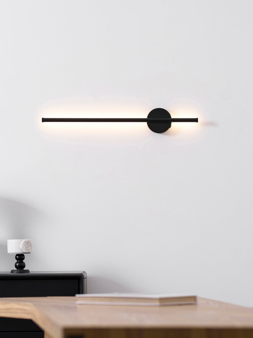 Lit warm above a nightstand, the beam falling onto the books stacked there