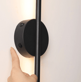 A hand touching the round hub to switch the bar on against a white wall