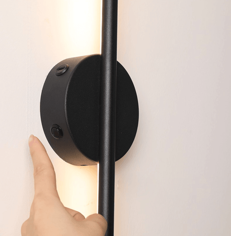 A hand touching the round hub to switch the bar on against a white wall