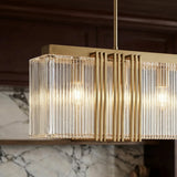 A long gold chandelier of ribbed clear shades lit in a row against a marble wall
