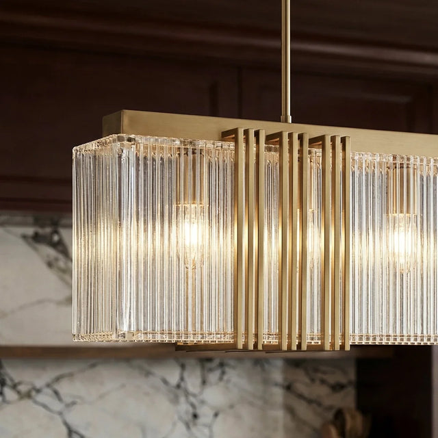 A long gold chandelier of ribbed clear shades lit in a row against a marble wall
