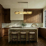 A lit bar above a kitchen island with stools and a stone counter