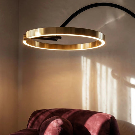 The lit gold ring hanging over a velvet armchair, the black arm rising behind