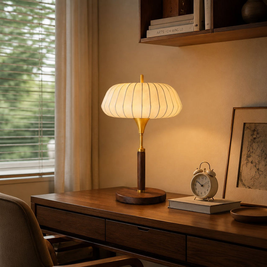 Remote control table lamp lit on a desk beside a clock and frames