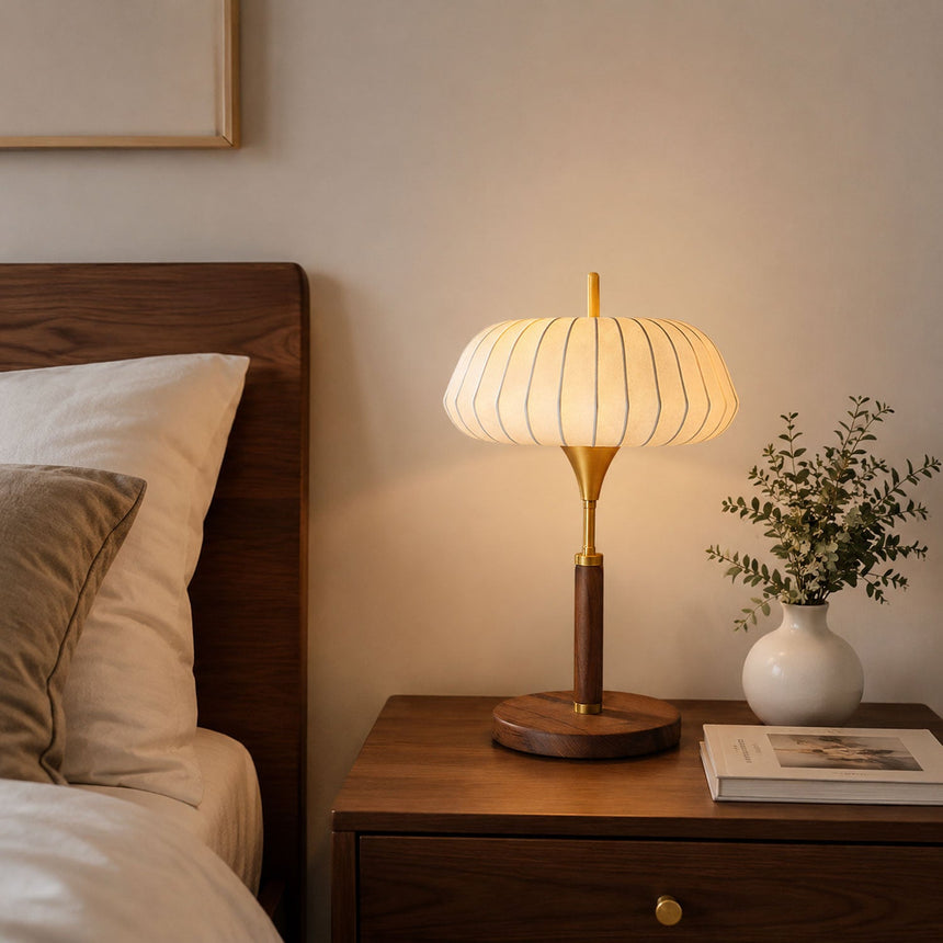 Remote control table lamp lit on a nightstand beside a made bed