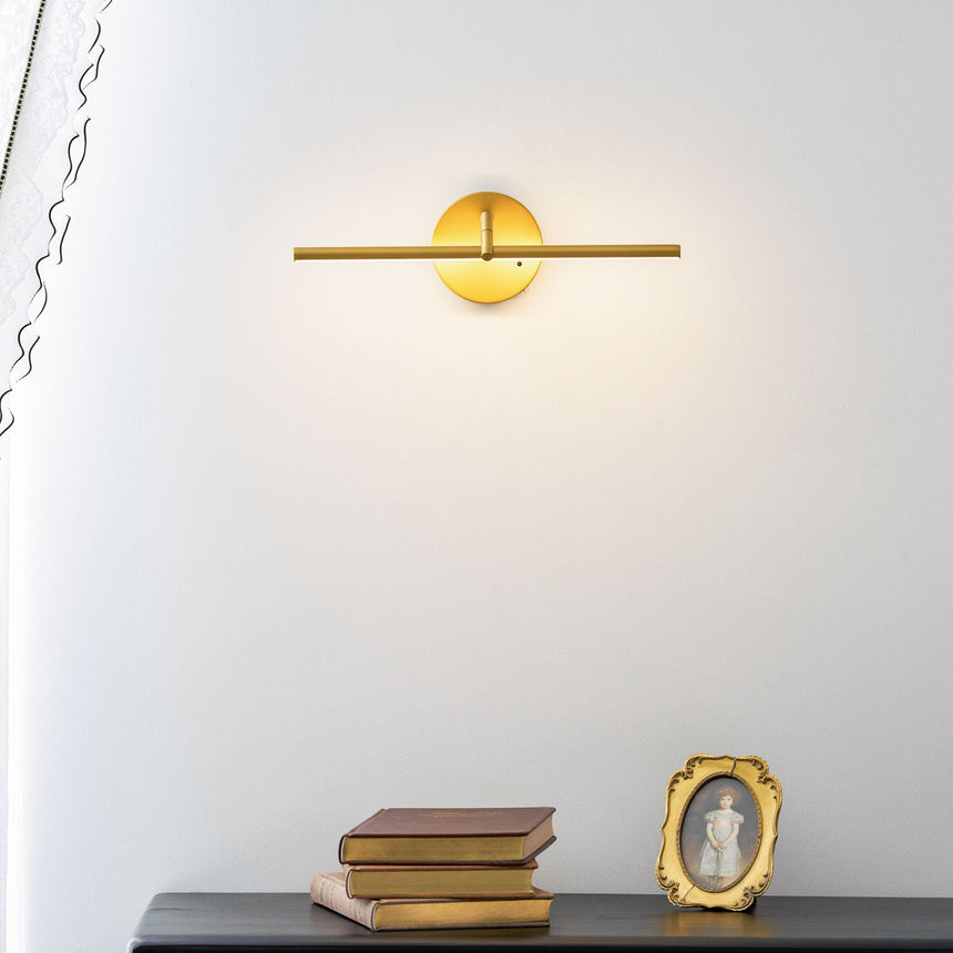 Gold arm lit above a black chest of drawers with books and a small gilt frame