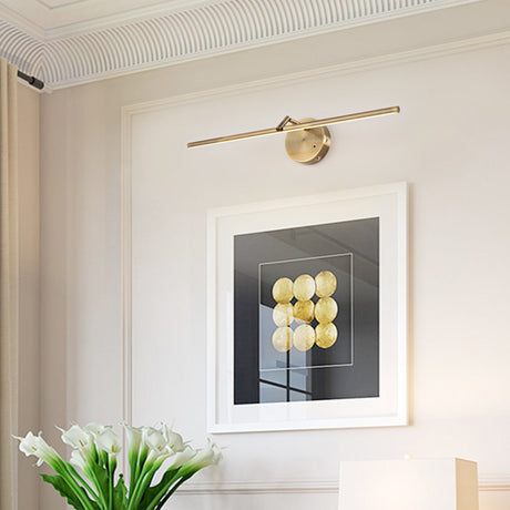 Gold arm lit above a framed print on a pale wall beside a vase of white tulips