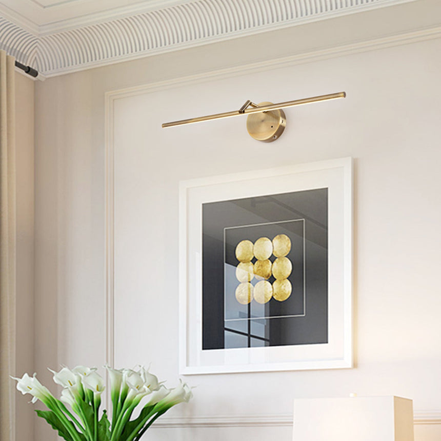 Gold arm lit above a framed print on a pale wall beside a vase of white tulips