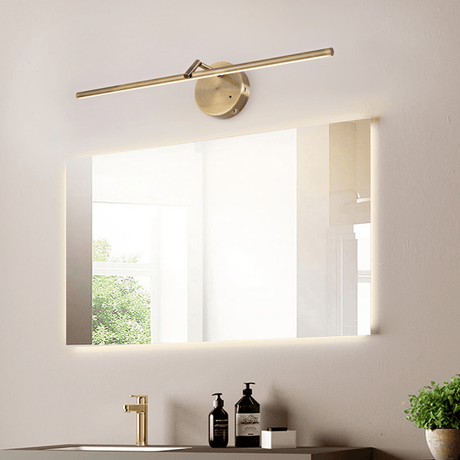 Gold arm lit above a wide bathroom mirror over a stone counter with a plant