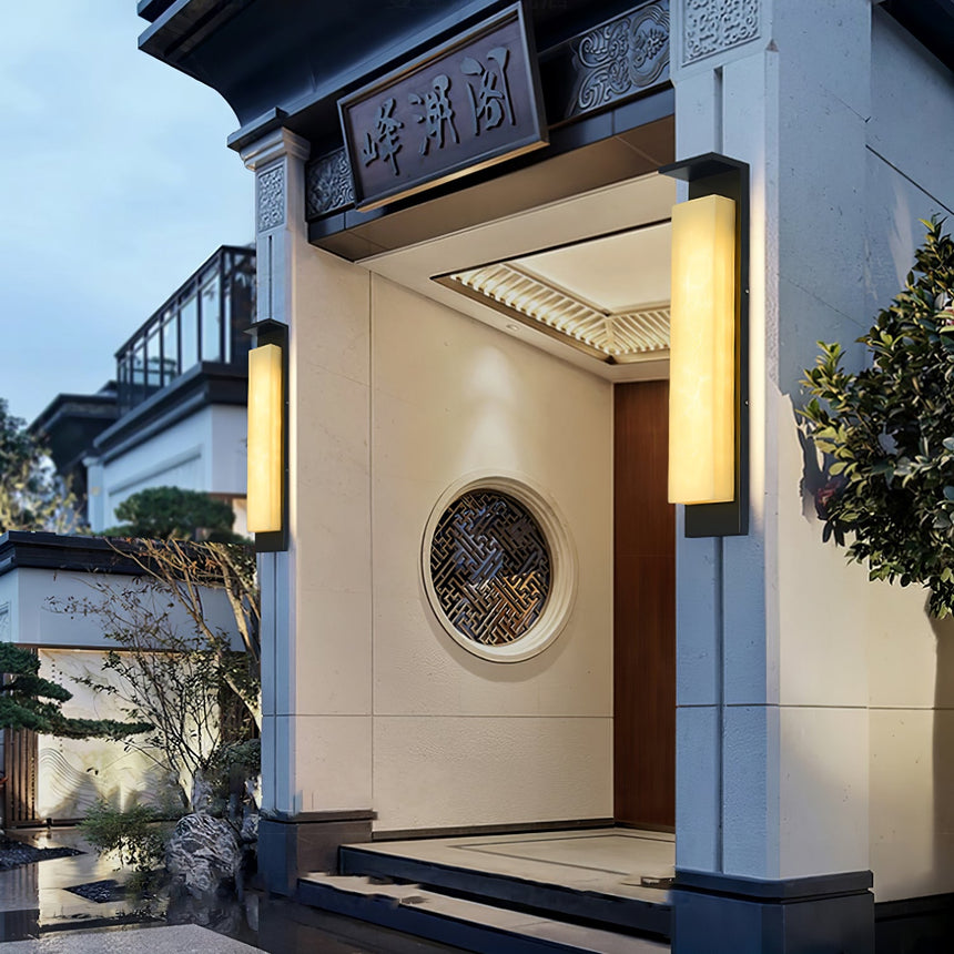 A panel light beside a courtyard entry with a round window in the far wall