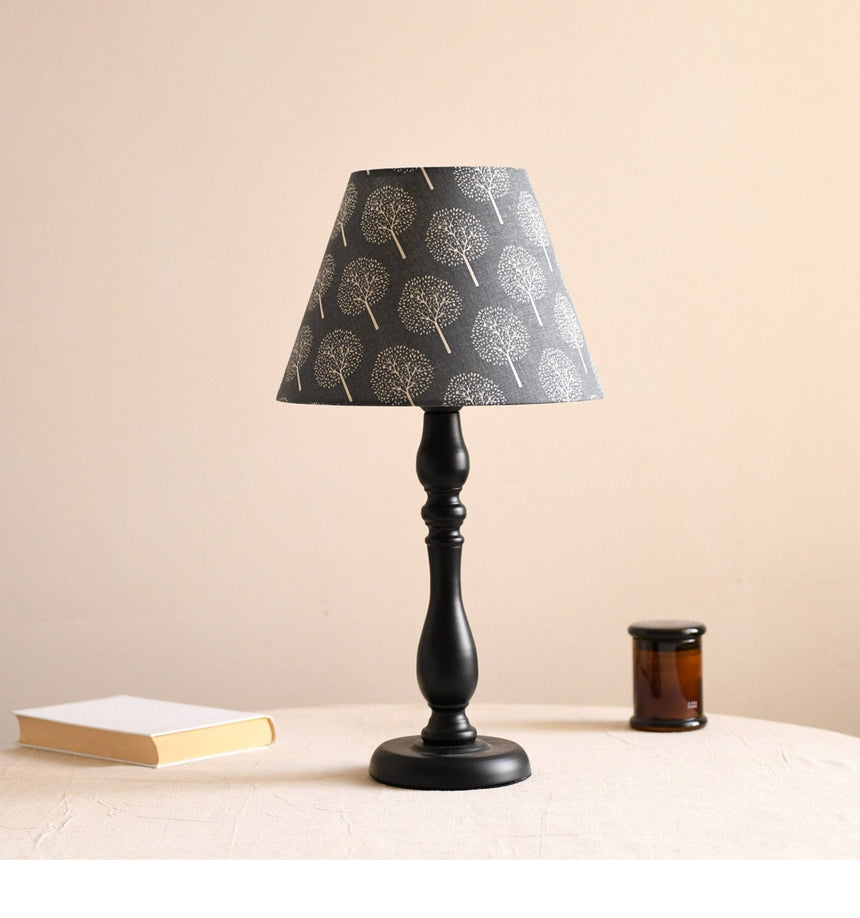 Table lamp with a dark shade printed with pale birch trees, lit