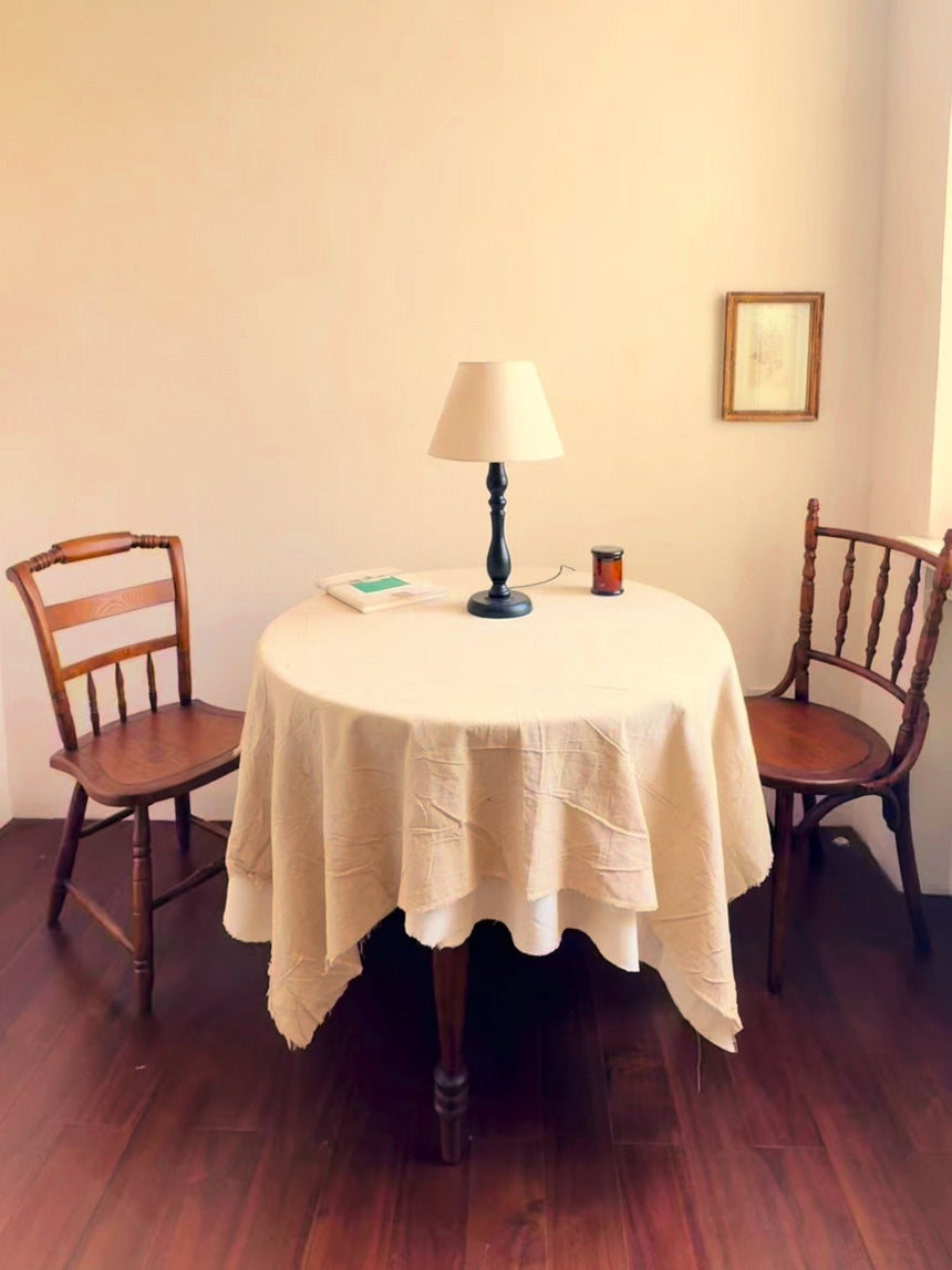 Table lamp lit on a round covered table between two wood chairs