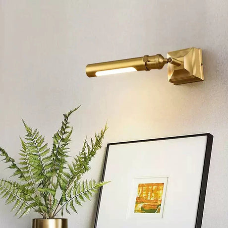 Brass tube lit above a framed picture, a fern leaning into the frame