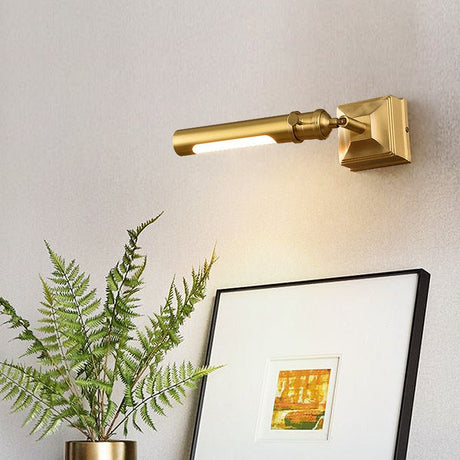 Brass tube lit above a framed artwork beside a fern in a brass planter
