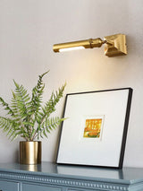 Brass tube lit above framed art with a fern and a blue cabinet below