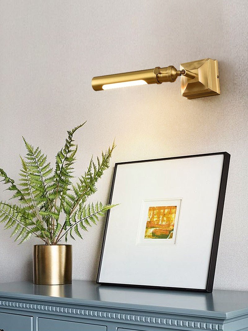 Brass tube lit above framed art with a fern and a blue cabinet below