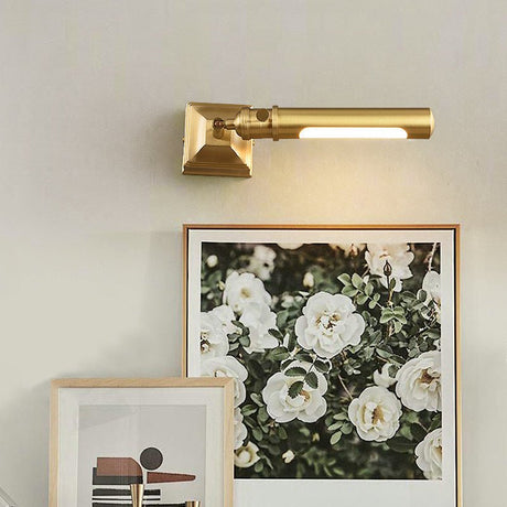 Brass tube lit over framed floral art leaning on a shelf beside a vase