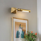Brass tube lit over a framed artwork with orange flowers in a green vase