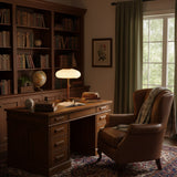 Ribbed glass table lamp lit on a desk in a room lined with books