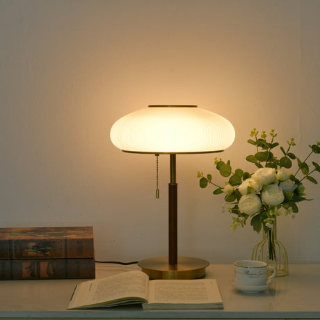 Ribbed glass table lamp lit against a soft blue ground with books