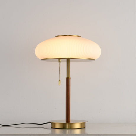 Ribbed glass table lamp lit against a plain pale ground
