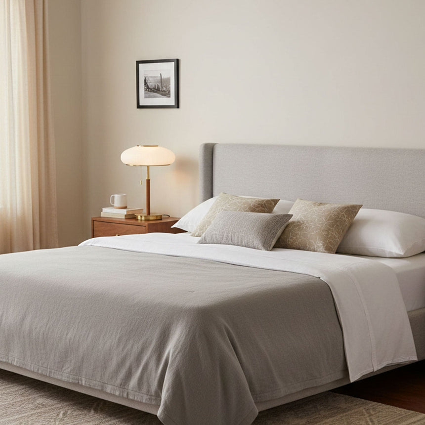 Ribbed glass table lamp lit on a nightstand beside a made bed