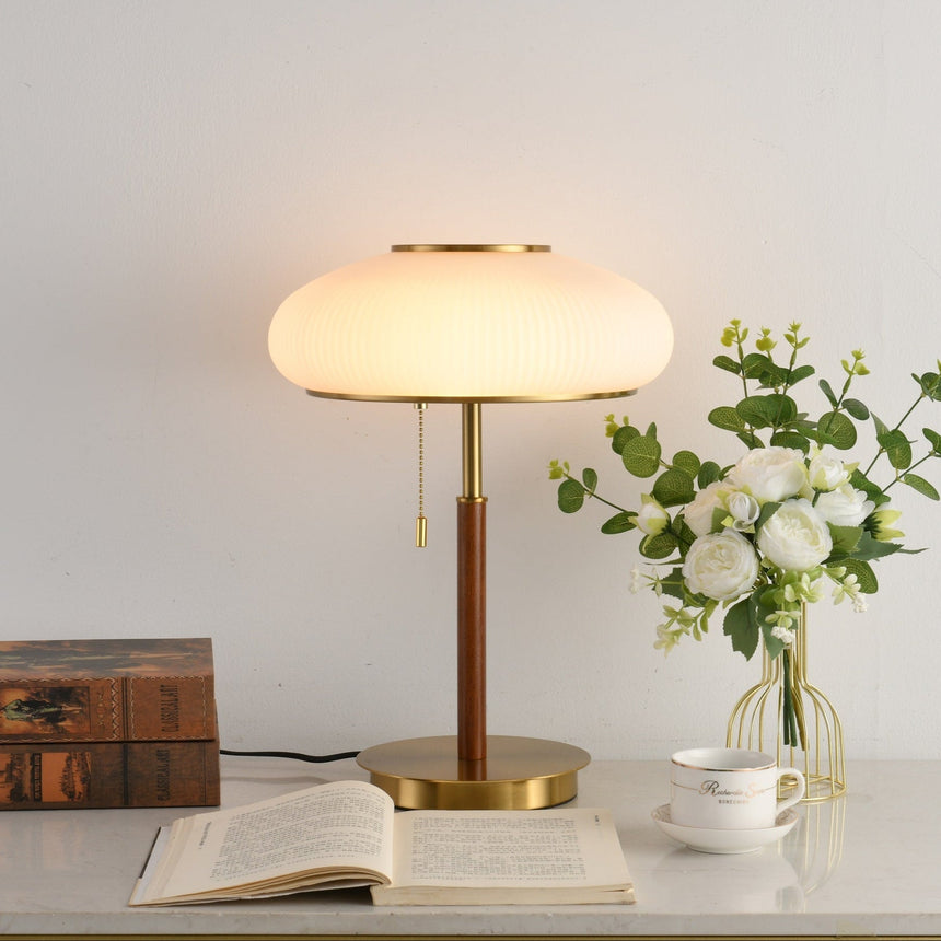 Ribbed glass table lamp lit beside an open book and a cup