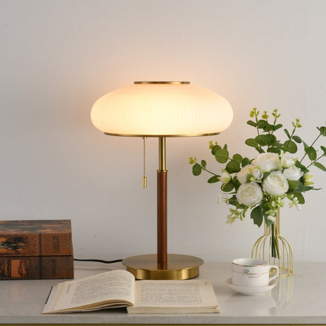 Ribbed glass table lamp lit beside a glass vase of white roses