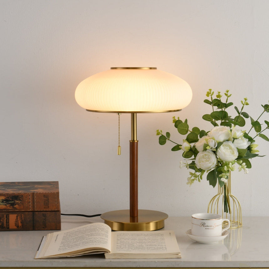 Ribbed glass table lamp lit beside a glass vase of white roses