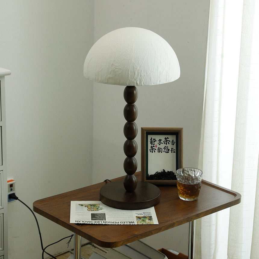 Rice paper table lamp lit on a table in the corner of a pale room