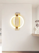 The sconce on a pale wall in a quiet room, a shelf and a vase below, window light on the floor