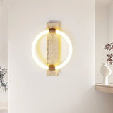 The travertine ring sconce lit on a white wall above a floating shelf with a white vase