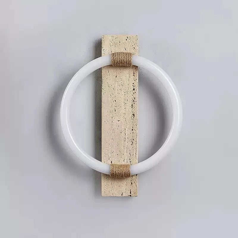 The sconce unlit, a white acrylic ring around a pale travertine slab with rope bands